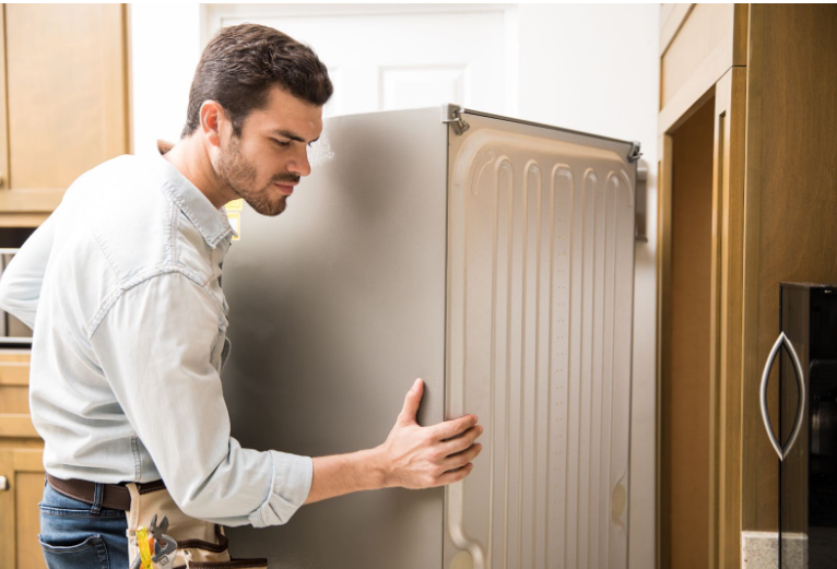 A technician inspecting the back of a refrigerator in a modern kitchen.
